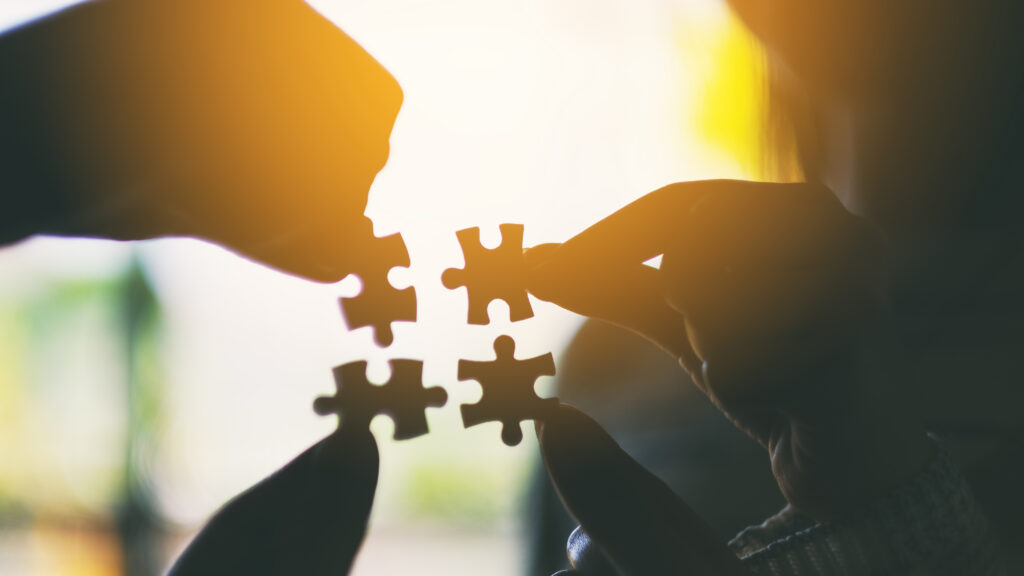 Silhouette image of many people holding and putting a piece of white jigsaw puzzle together
